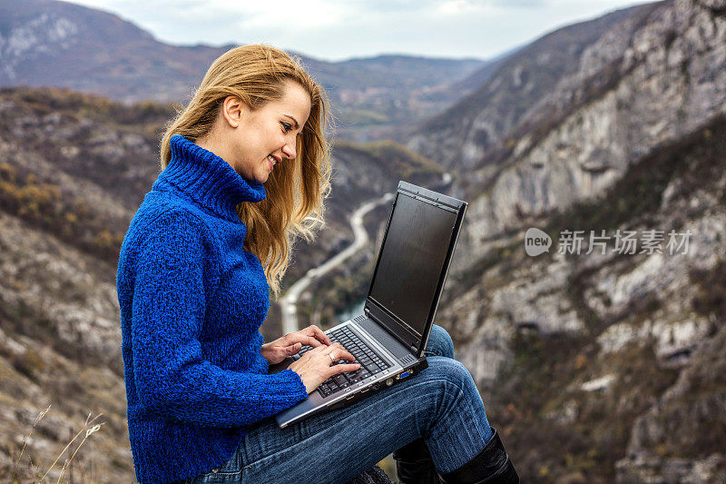 Young hiker using her laptop while sitting on top of a mountain